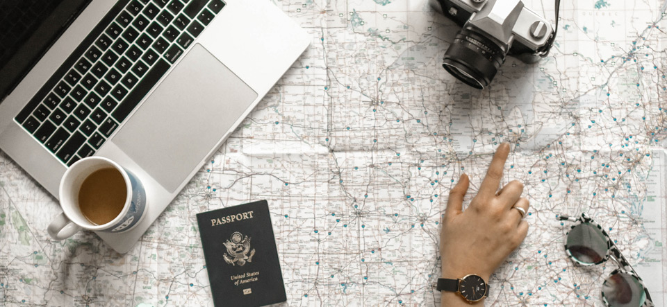 Person viewing a map with laptop, passport, and camera on table