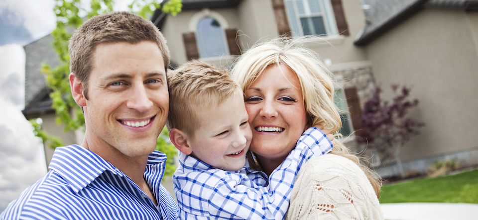 A stock photo of a beautiful young family in front of their modern home.