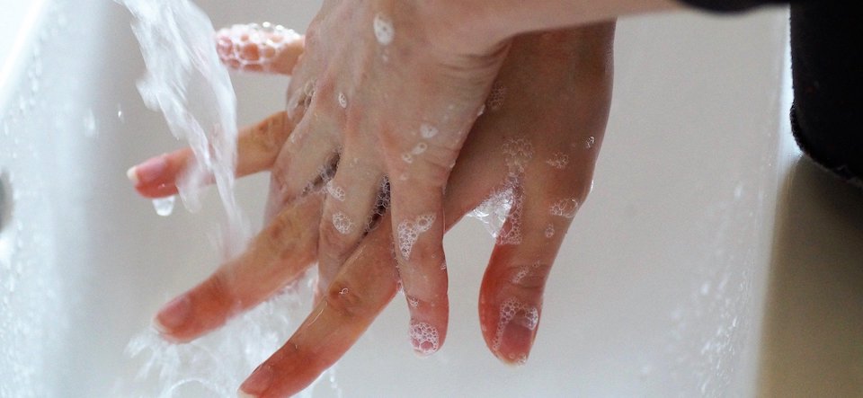 A person rinsing soapy hands with water