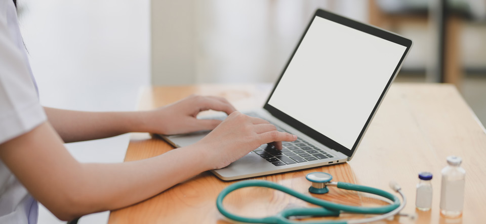 Medical professional using a laptop with a stethoscope and bottles on the table