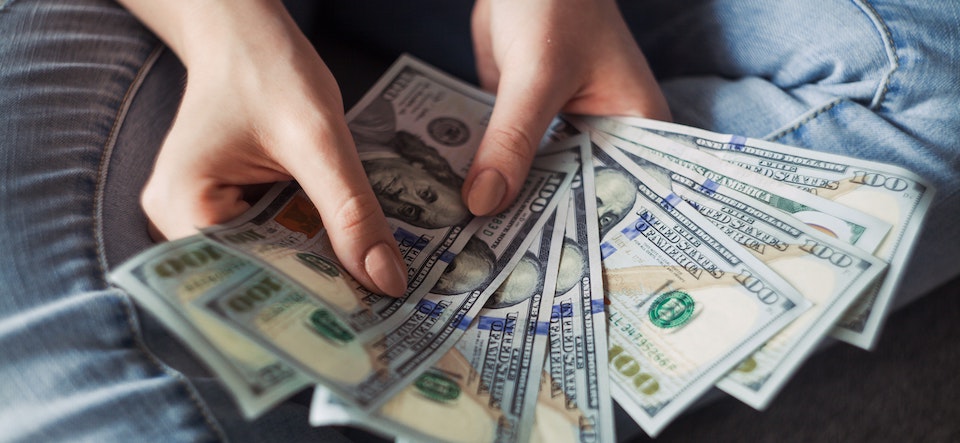 Person sitting and holding hundred dollar bills