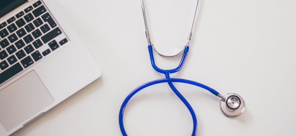 Stethoscope lying on a desk next to a laptop