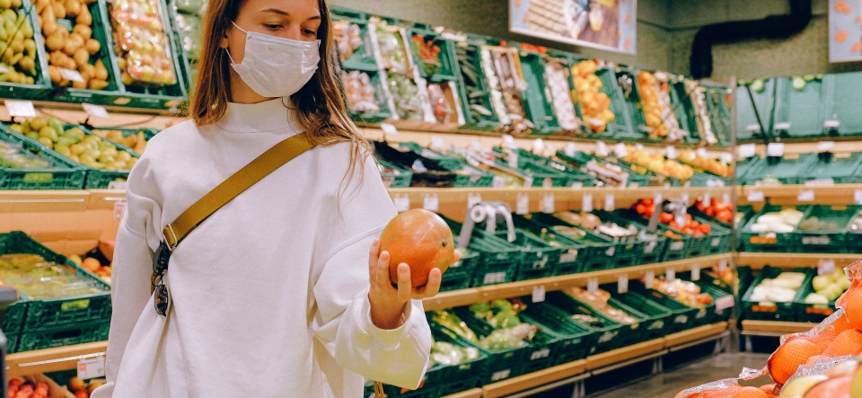 Woman wearing a surgical mask standing in a grocery store holding a grapefruit