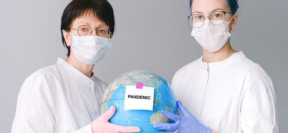 Two health workers holding a globe with a pandemic sign on it
