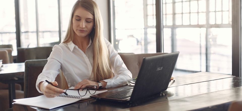 young adult professional woman writing in a notebook in front of a laptop