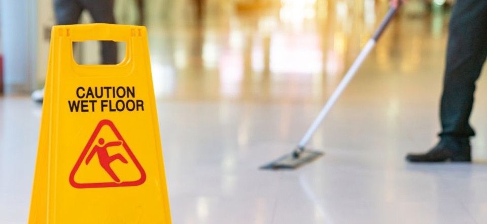 Employee mopping a floor with a warning sign placed