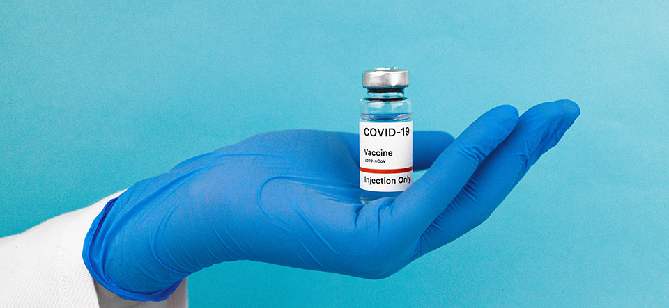 Doctor's gloved hand holding a vial of COVID-19 vaccine