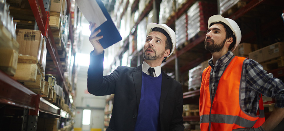 Two supervisors discussing amount of goods for export on shelves of warehouse