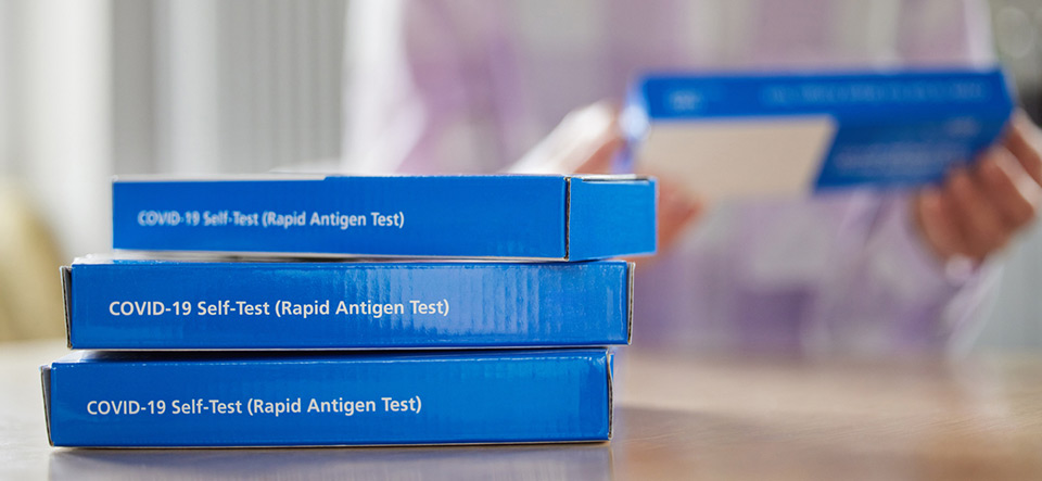 Close Up Of Woman At Home Reading Instructions On Supply Of Covid-19 Rapid Antigen Self-Testing Kits