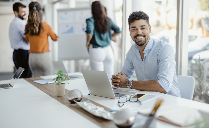 Horizontal portrait of a smiling african american office working man looking at camera with colleagues in the background.