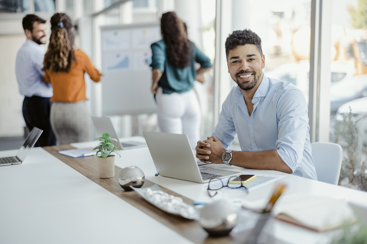 Horizontal portrait of a smiling african american office working man looking at camera with colleagues in the background.