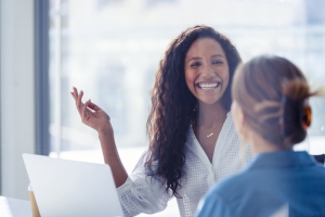 Business colleagues having a conversation. They are both young business people casually dressed in a modern office. Could be an interview or consultant working with a client. She is listening and smiling. One person has her back to us. Mixed ethnic group. One is African American and the other is Caucasian