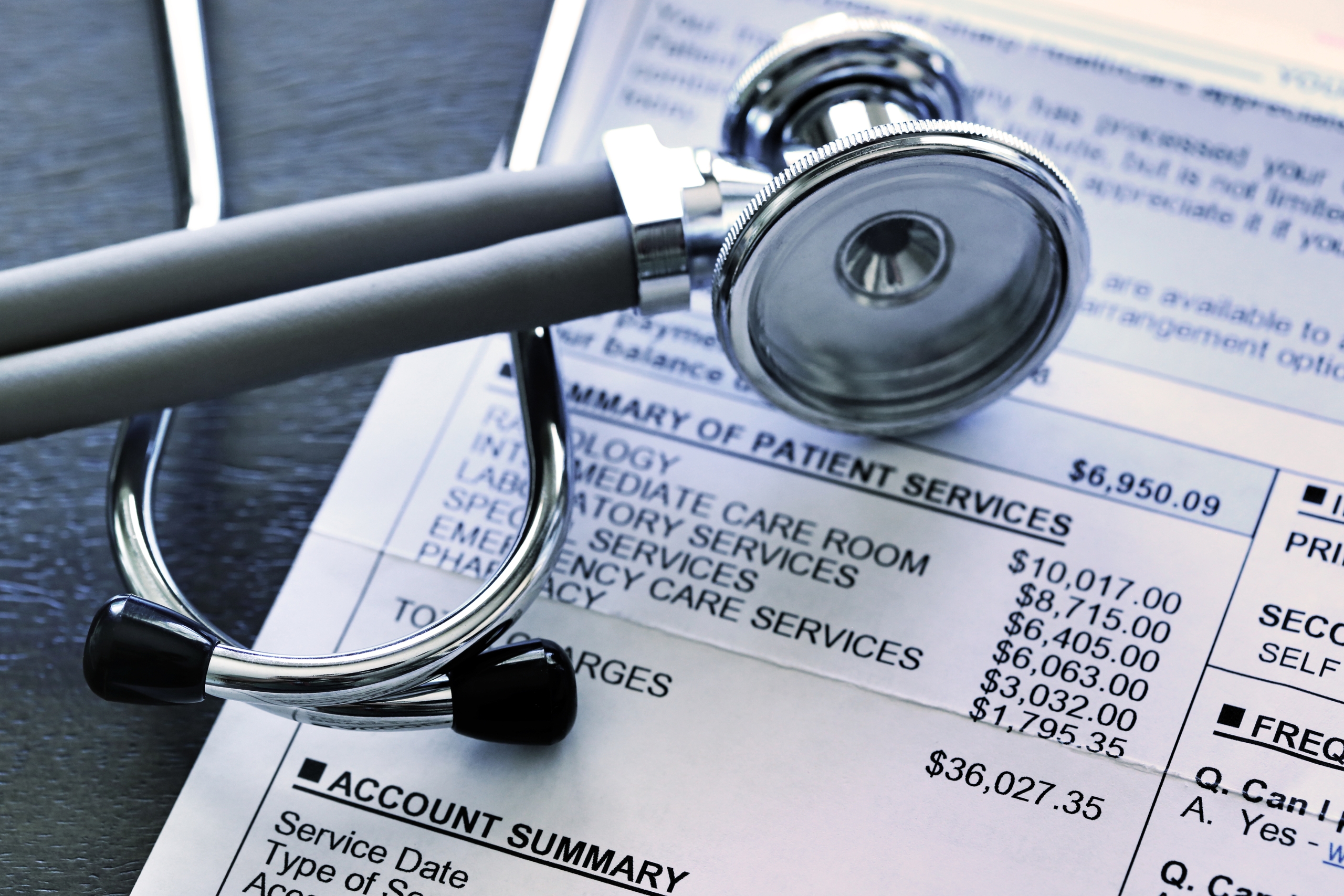 A stethoscope rests on top of a very expensive medical invoice that has line items for different services provided.