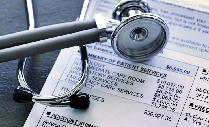 A stethoscope rests on top of a very expensive medical invoice that has line items for different services provided.