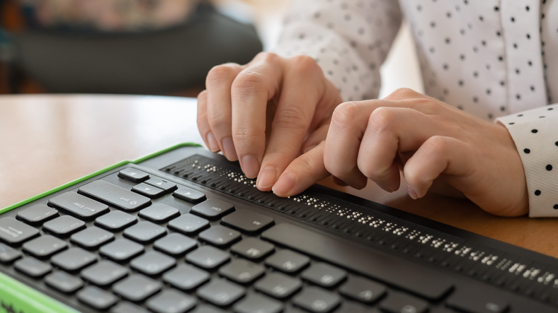 A blind woman uses a computer with a Braille display and a computer keyboard. Inclusive device