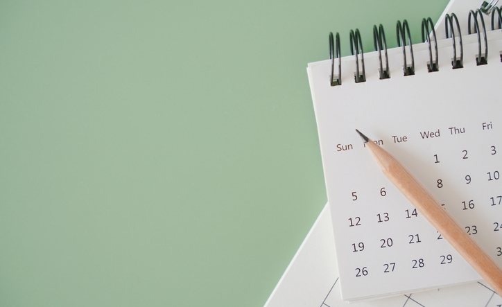 top view of white calendar and sharpen brown pencil on green background, schedule, timeline, planning concept