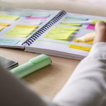 Close-up of agenda organize with color coding sticky notes for time management. Productive schedule for appointments and reminders. Hand holding a yellow highlighter marker. Organization and planning