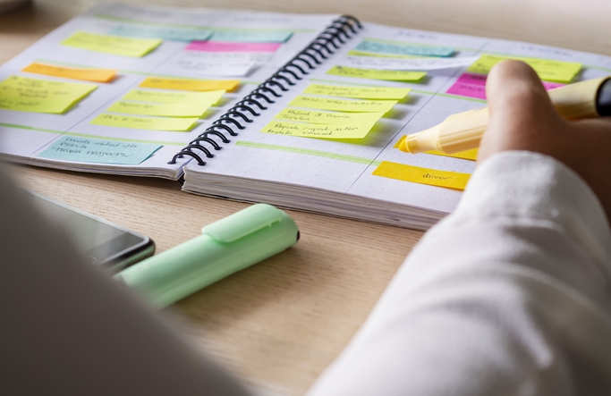 Close-up of agenda organize with color coding sticky notes for time management. Productive schedule for appointments and reminders. Hand holding a yellow highlighter marker. Organization and planning