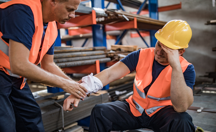 Manual worker feeling pain after having an injury at work while his colleague is helping him.