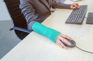 woman with broken hand and green cast working on computer in office.