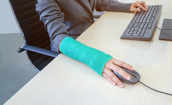 woman with broken hand and green cast  working on computer in office.