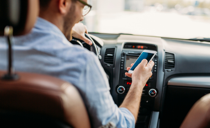 Man looking at mobile phone while driving a car.