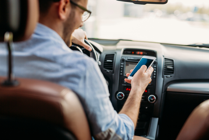 Man looking at mobile phone while driving a car.